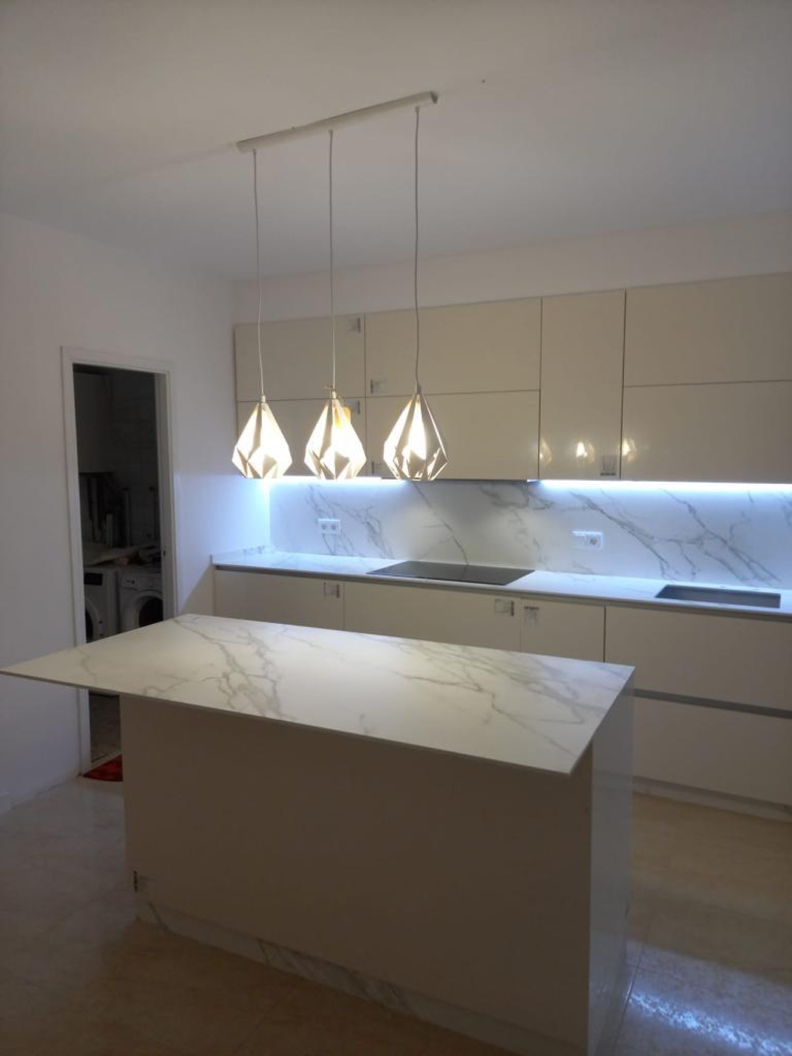 Cocina reformada con isla de mármol y luz de suspensión en Barcelona